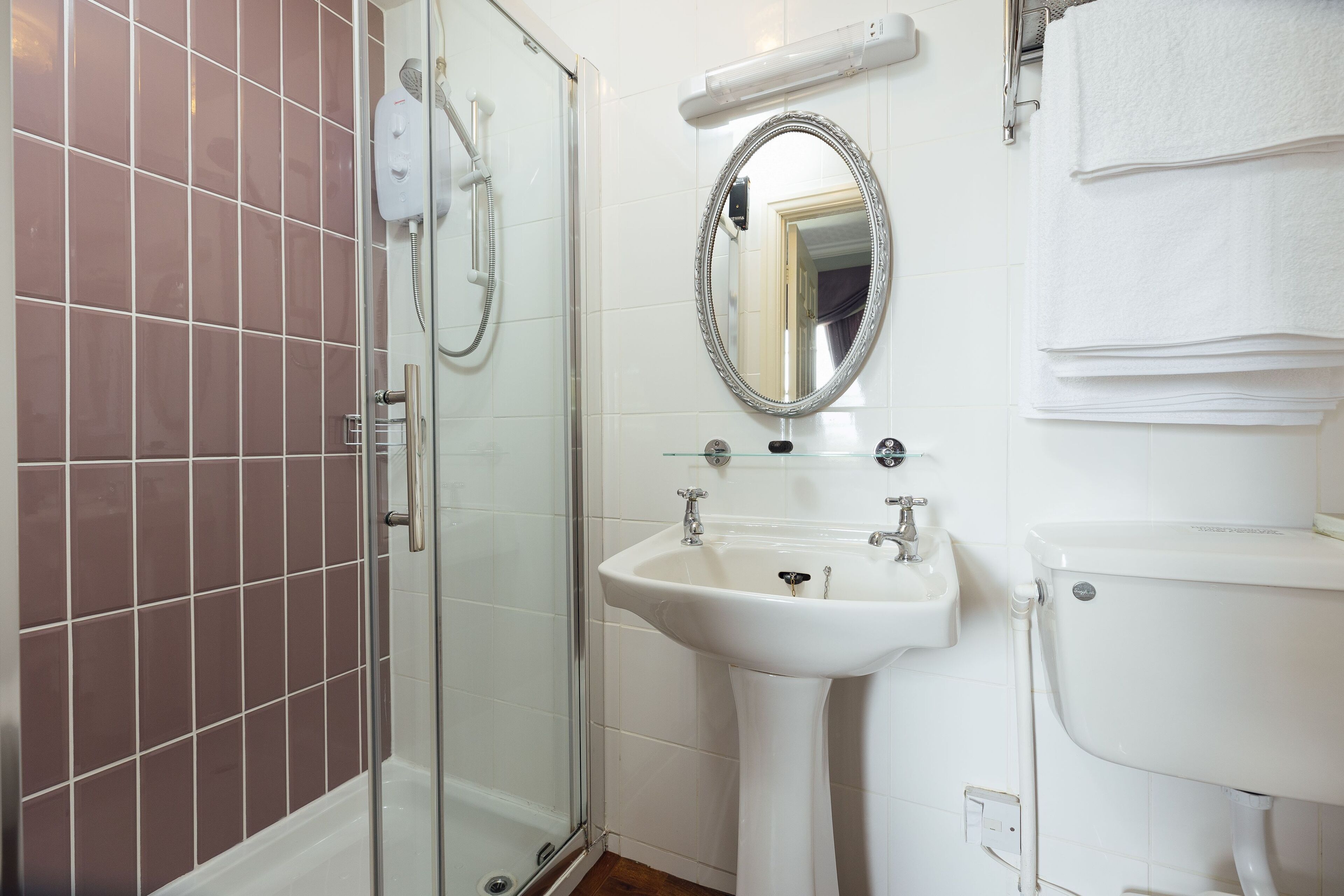 Un baño con cabina de ducha de vidrio, lavamanos pedestal, inodoro y espejo sobre el lavamanos.