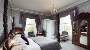A bedroom with a large bed, a wooden wardrobe, a desk with a lamp, and a chair. - Elm Grove Country House (Tenby)