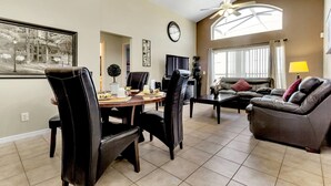 A spacious living room with a dining area, a large window, and a ceiling fan.
