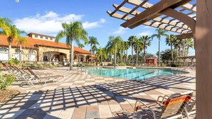 A pool area with sun loungers, a clear pool, and a building with a red roof in the background.