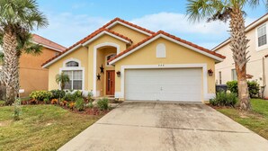 A two-story house with a red-tiled roof, a garage, and a well-maintained front yard with palm trees and colorful plants. - Aviana Resort - Lovely 4bd/3ba Pool Home- #4525 (Davenport)