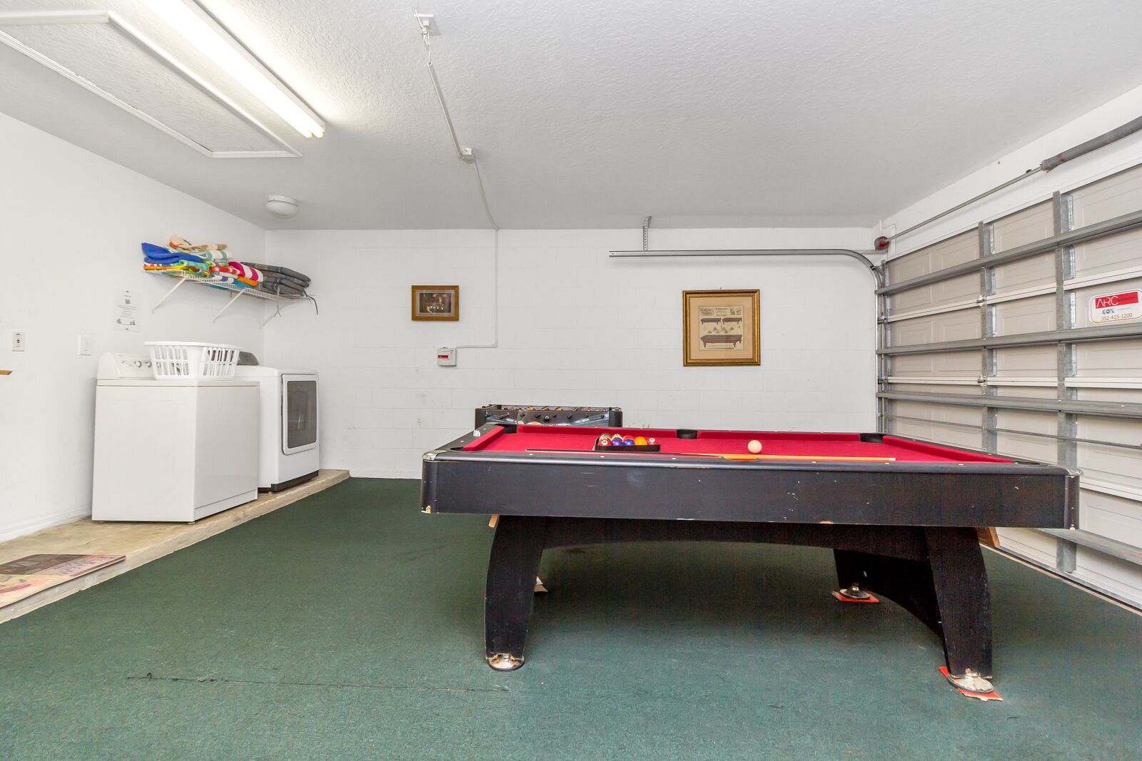 A pool table in a room with a laundry area, a small refrigerator, and a garage door.