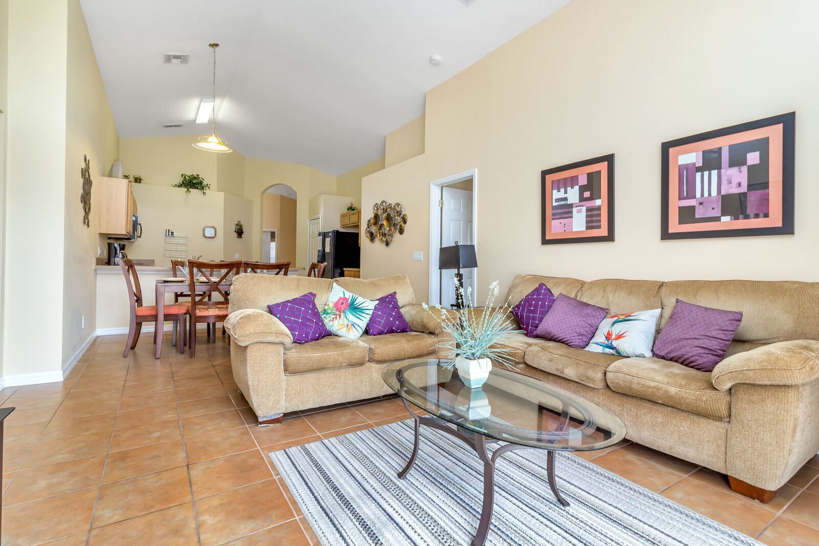 A spacious living area with two beige sofas, a glass coffee table, and a striped rug.