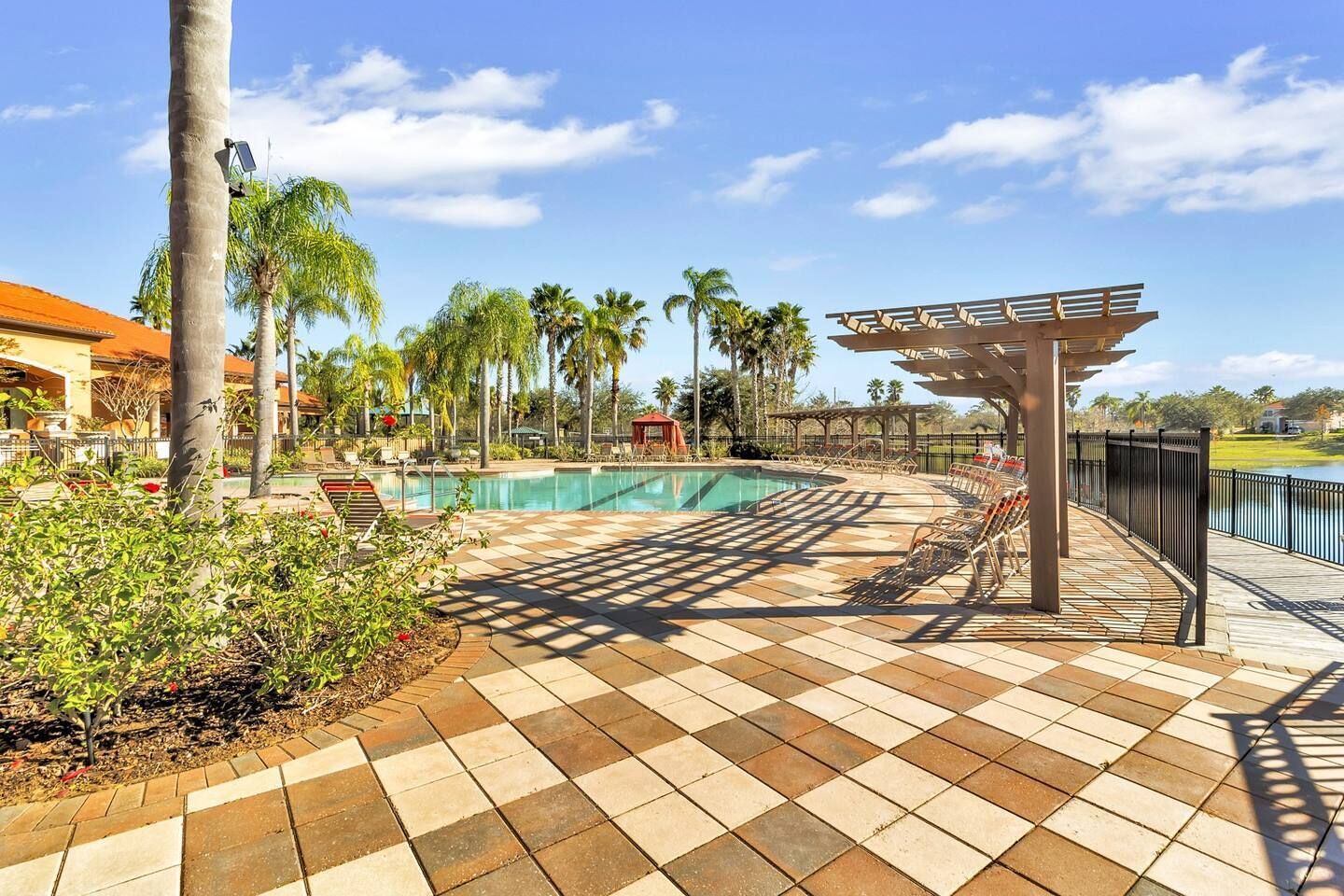 A pool area with a tiled deck, lounge chairs, and a pergola.