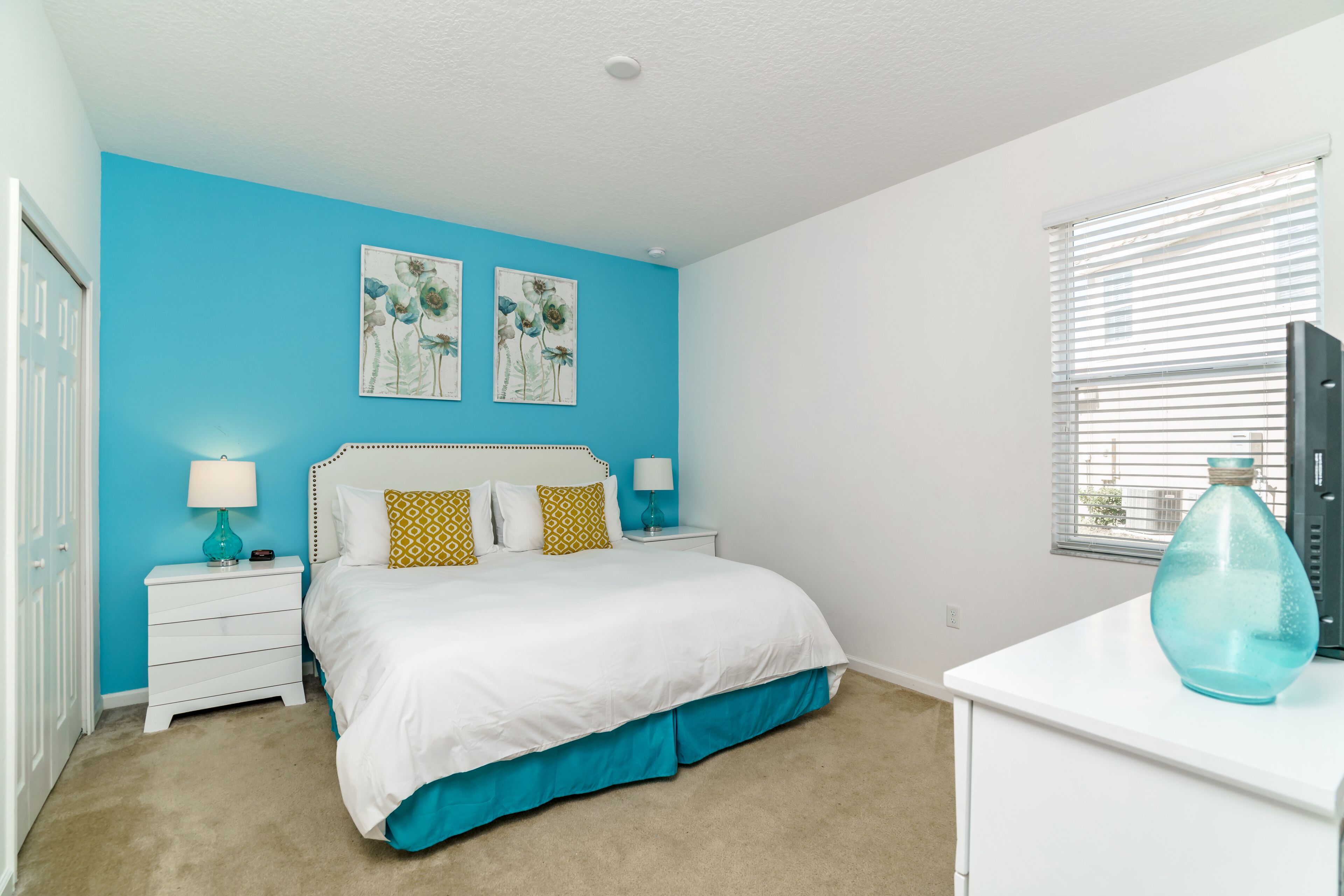 A bedroom with a bed, two nightstands, a dresser, and a window with blinds.