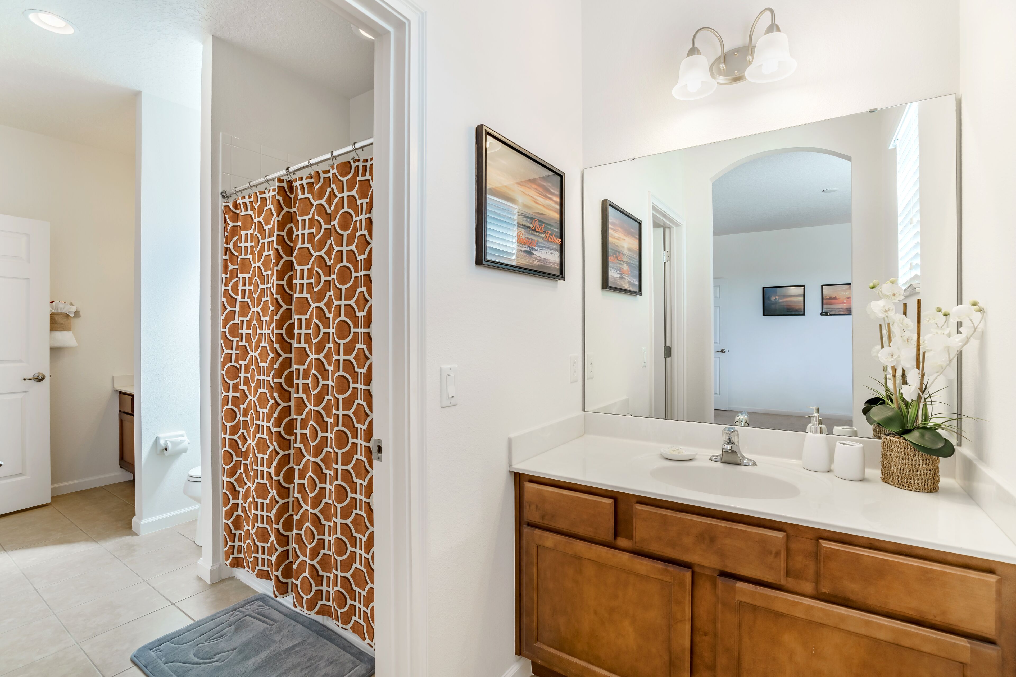 A bathroom with a shower, a large mirror, a sink with a vanity, and a door leading to another room.