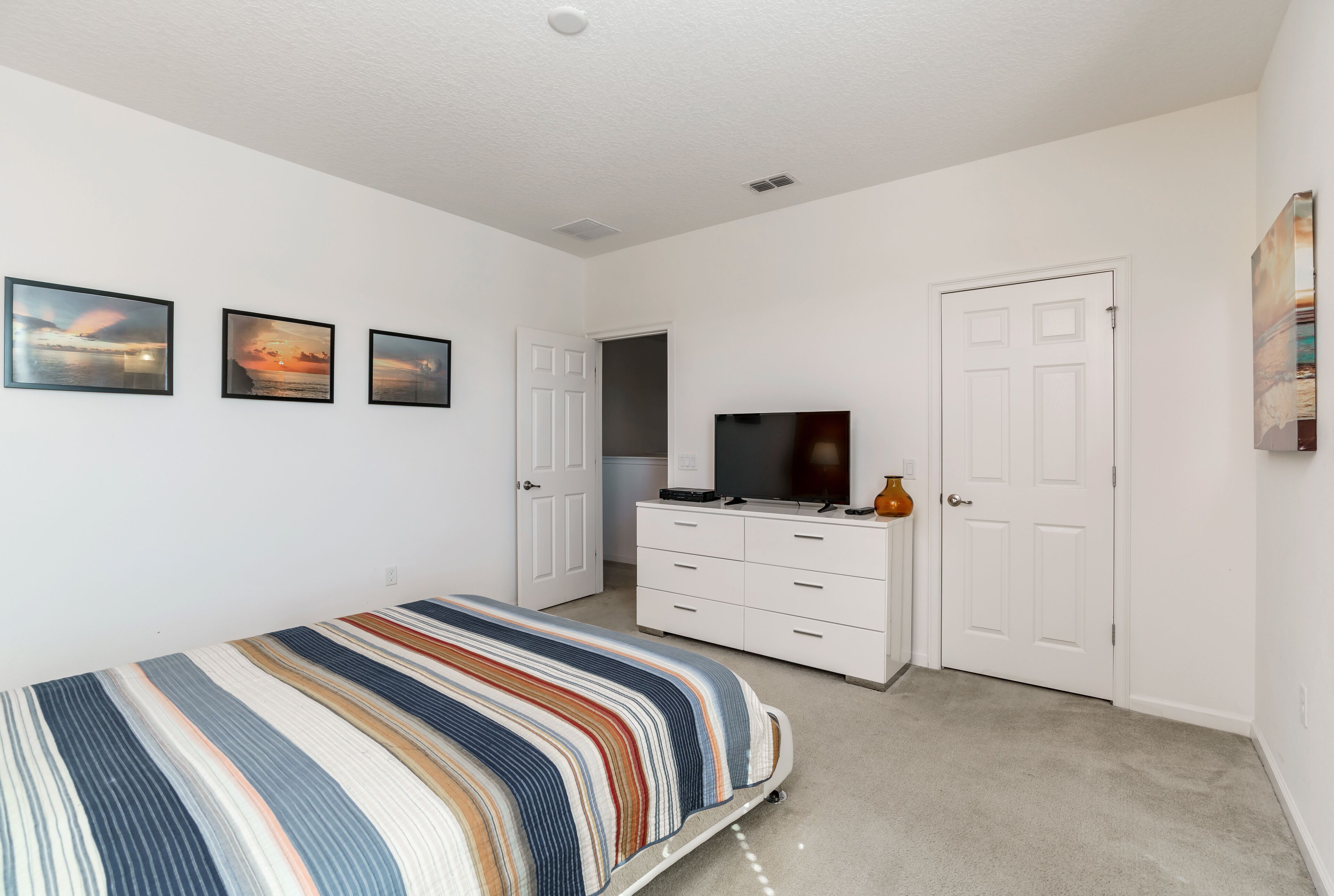 Une chambre à coucher avec un lit, une commode, un téléviseur et trois tableaux encadrés accrochés au mur.