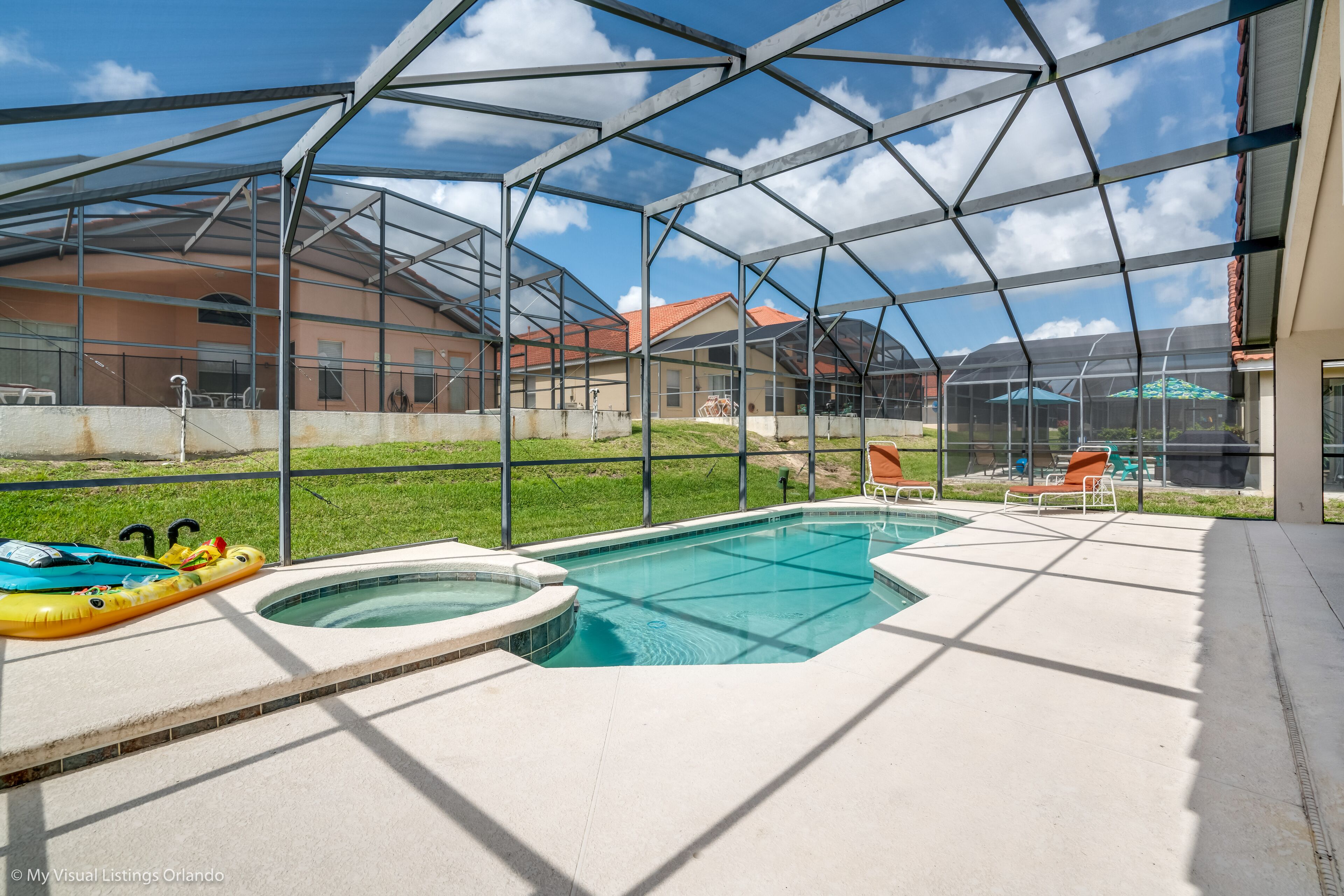 A covered outdoor swimming pool with a hot tub, surrounded by lounge chairs and a clear view of the neighborhood.