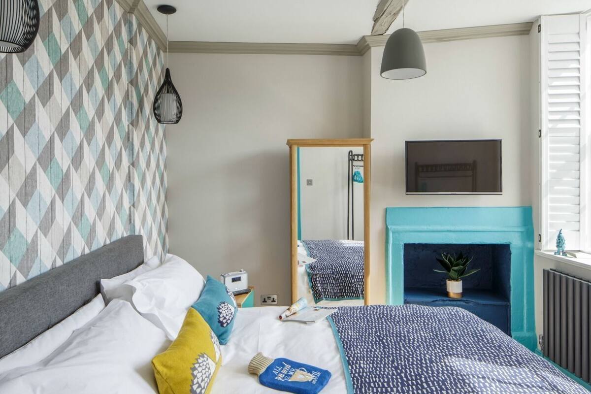 A bedroom with a bed, a mirror, a fireplace, and a television.