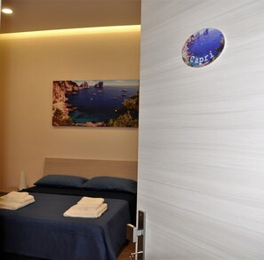 A hotel room with a bed, a painting of a coastal scene, and a circular sign with the word "Capri". - Le Tre Gemme (Pompei)