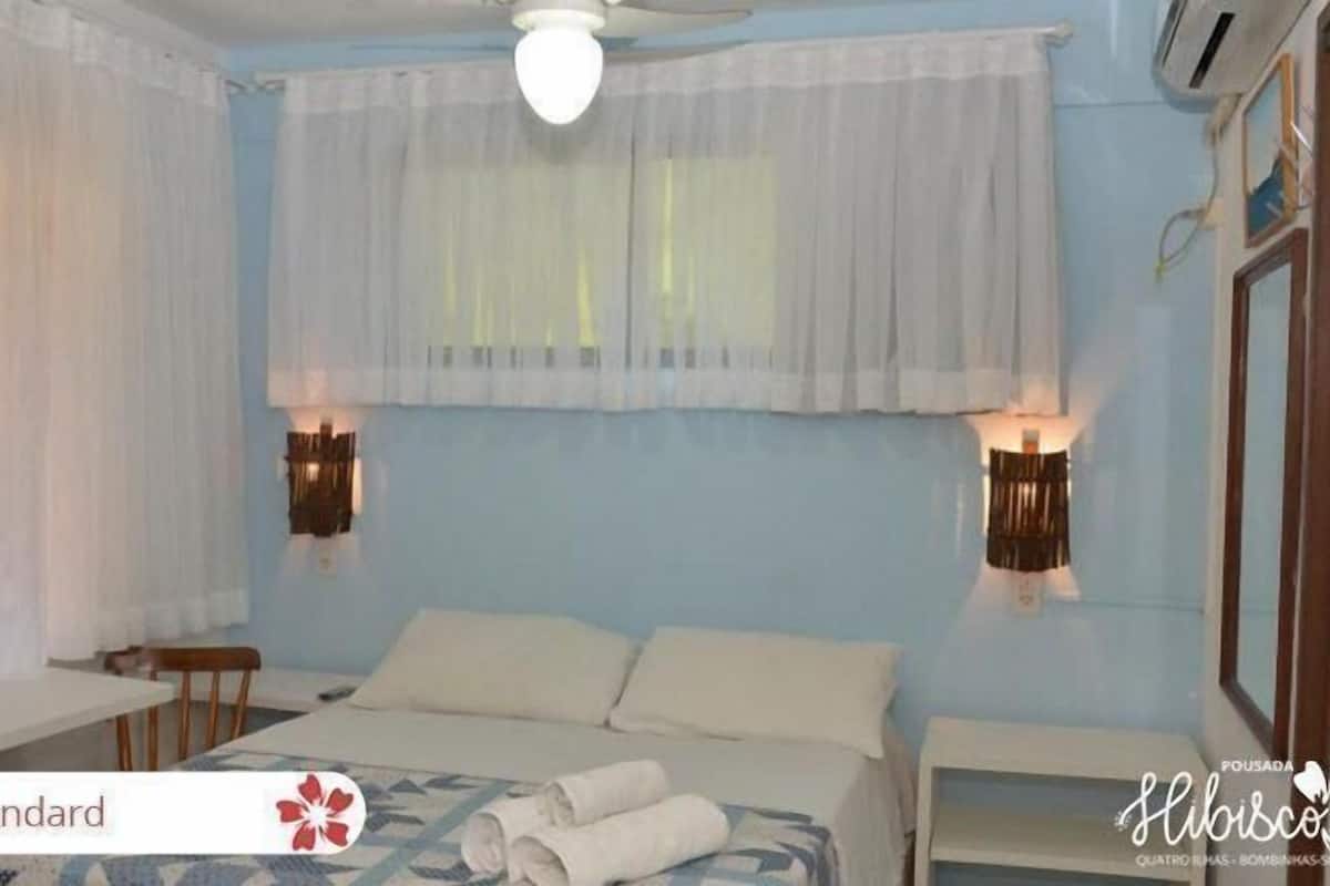 Habitación estándar con cama, una mesita, ventilador de techo y dos lámparas de pared.