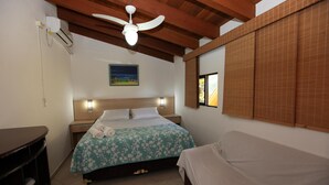 Une chambre d’hôtel avec un lit, des tables de chevet, un ventilateur de plafond, un tableau et une fenêtre avec des stores en bambou.