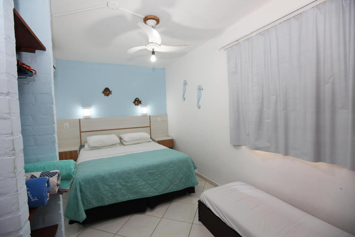 Un dormitorio con cama, mesita de noche, ventilador de techo y ventana con cortinas.