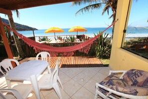 Une terrasse avec un hamac, des chaises en plastique blanches et une table. On y trouve deux parasols jaunes et une vue sur l’océan.