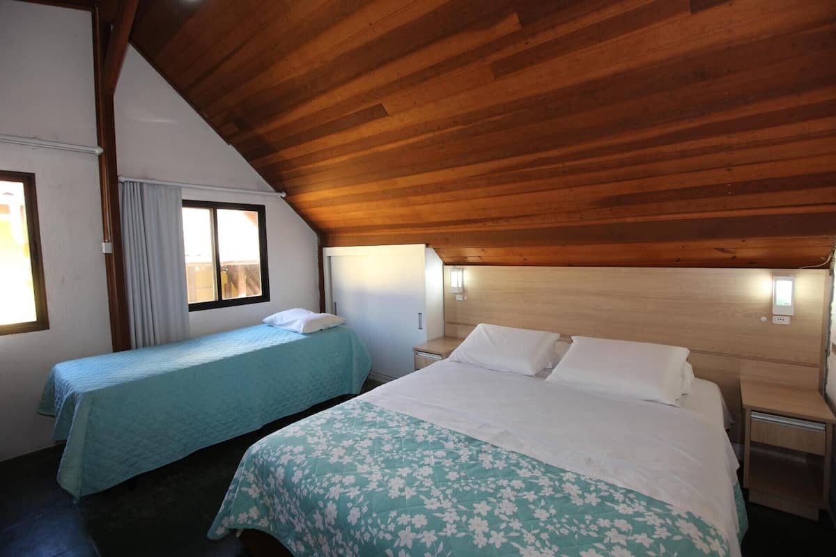 Una habitación con dos camas, techo de madera y una ventana con cortinas.