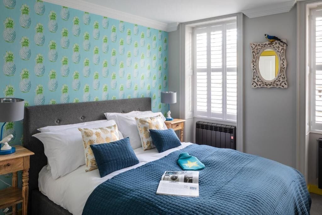 Un dormitorio con cama, mesita de noche, lámpara, espejo y ventana con persianas.