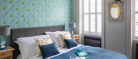 Un dormitorio con cama, mesita de noche, lámpara, espejo y ventana con persianas.