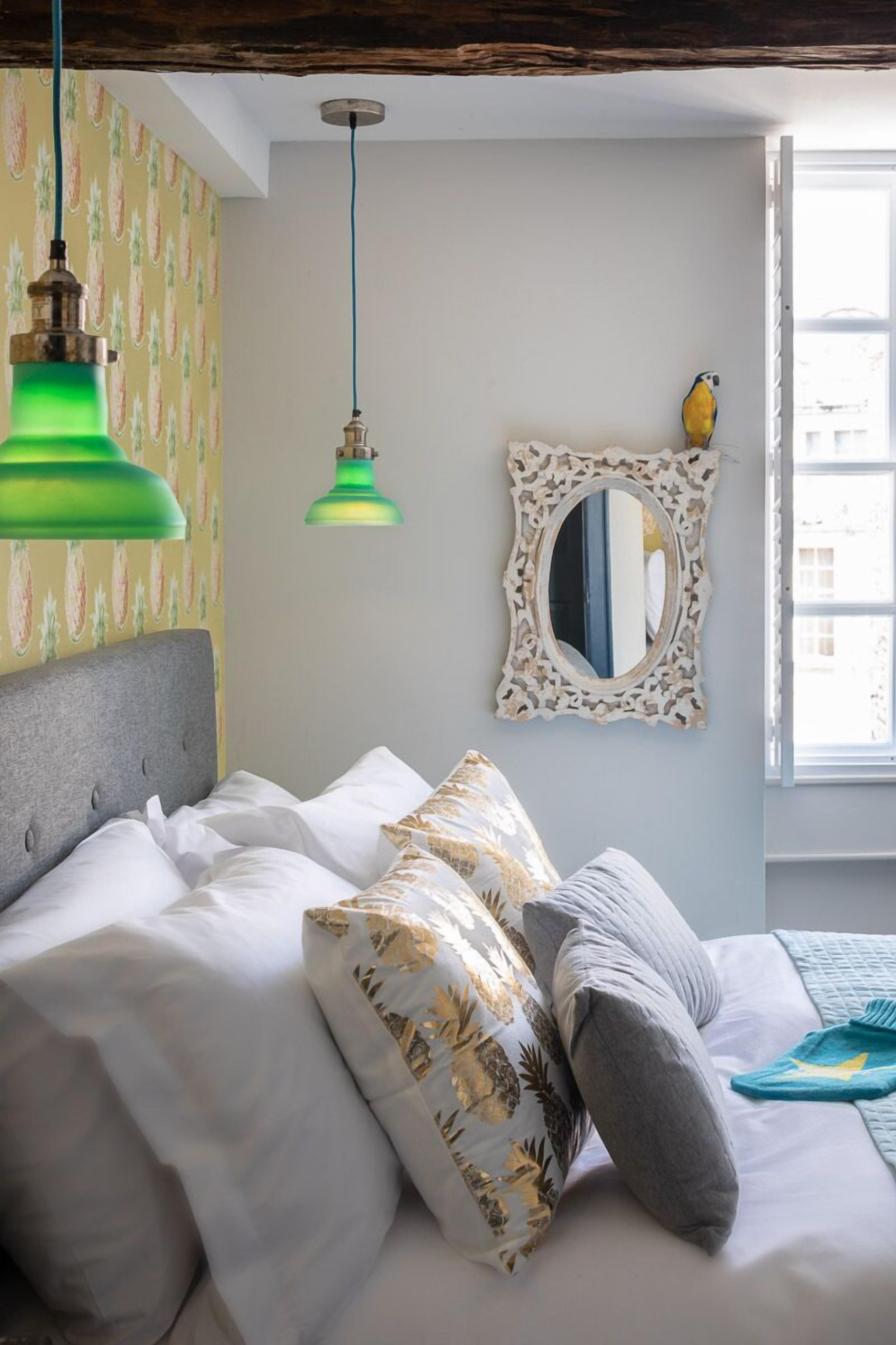 Een slaapkamer met een bed, kussens, een spiegel en een raam.