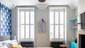 Quarto com cama, duas janelas, radiador, mesa pequena e lareira.
