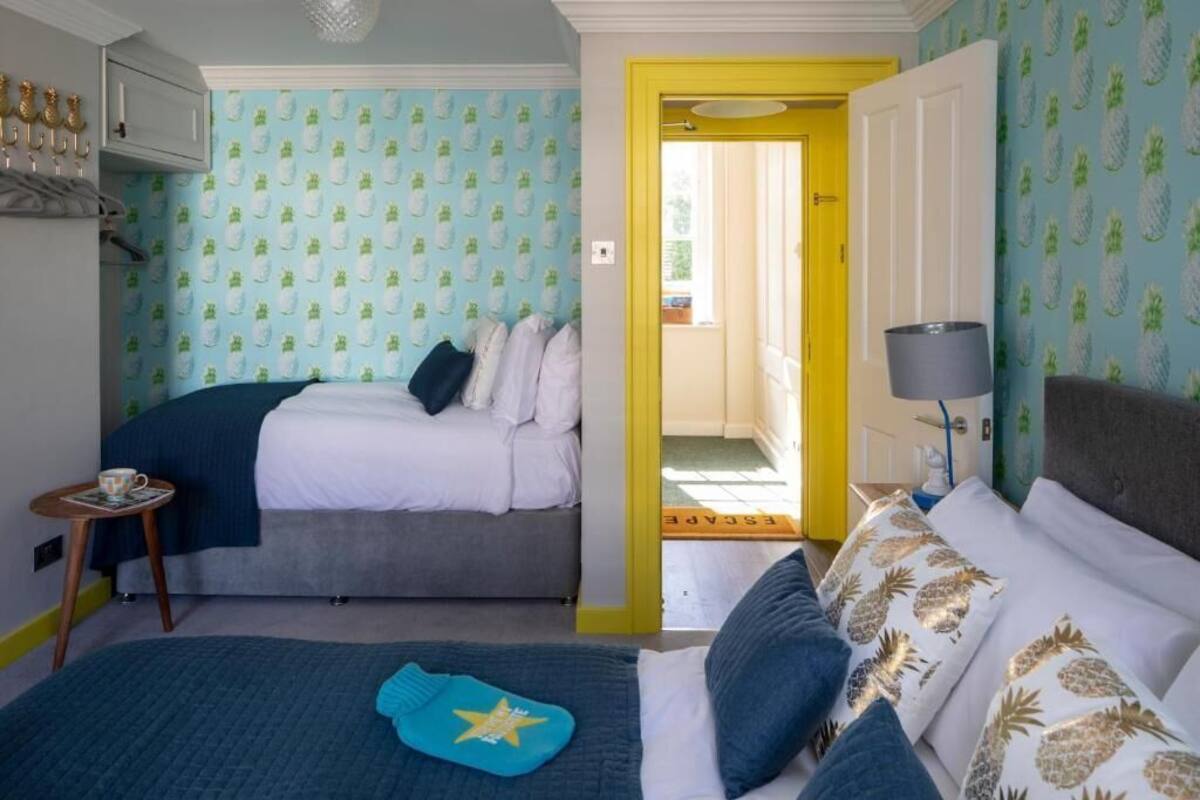 Un dormitorio con dos camas, una mesita con una taza y una puerta que da a otra habitación.