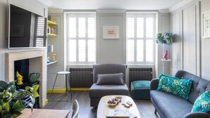 Uma sala de estar acolhedora com lareira, um sofá, uma mesa de centro e uma TV fixada na parede.
