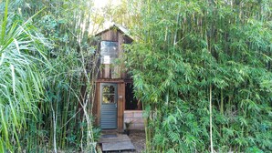 A rustic wooden cabin with a small porch, surrounded by dense bamboo and other greenery. - Sítio Sapiranga (Sapiranga)