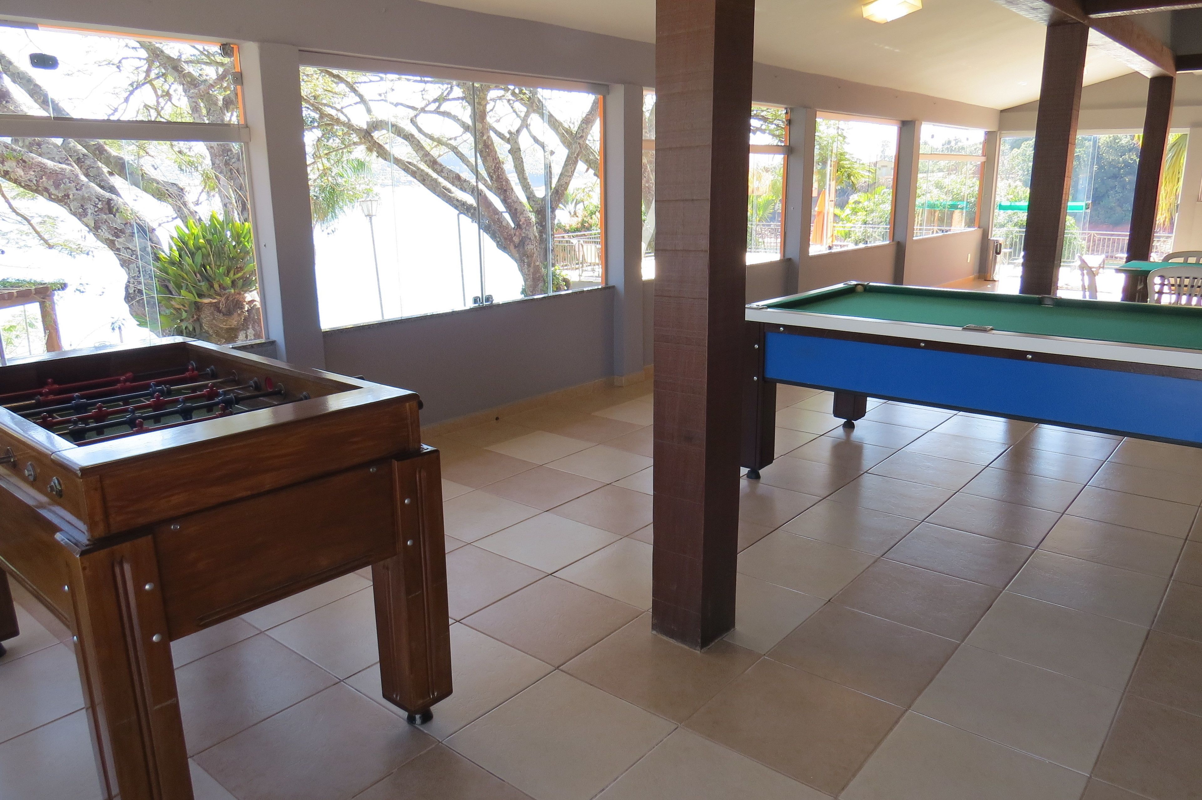 Une pièce avec un baby-foot et une table de billard, de grandes fenêtres donnant sur la verdure et un balcon.