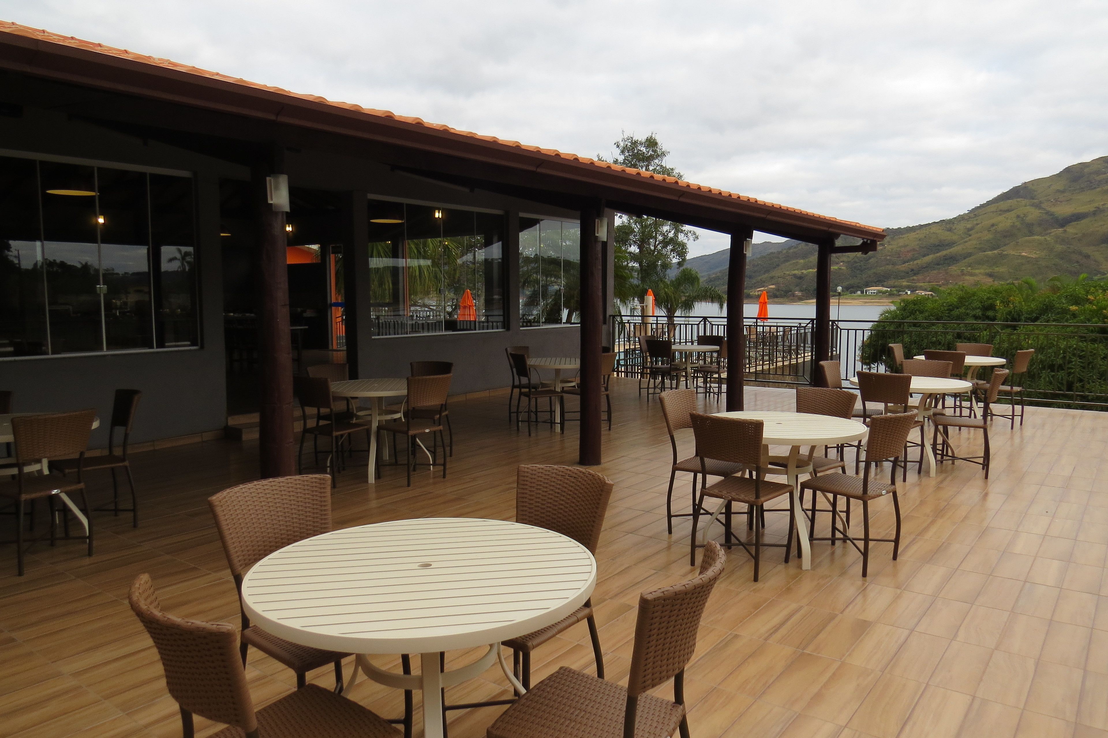 An outdoor patio with round tables and wicker chairs, overlooking a body of water and hills.