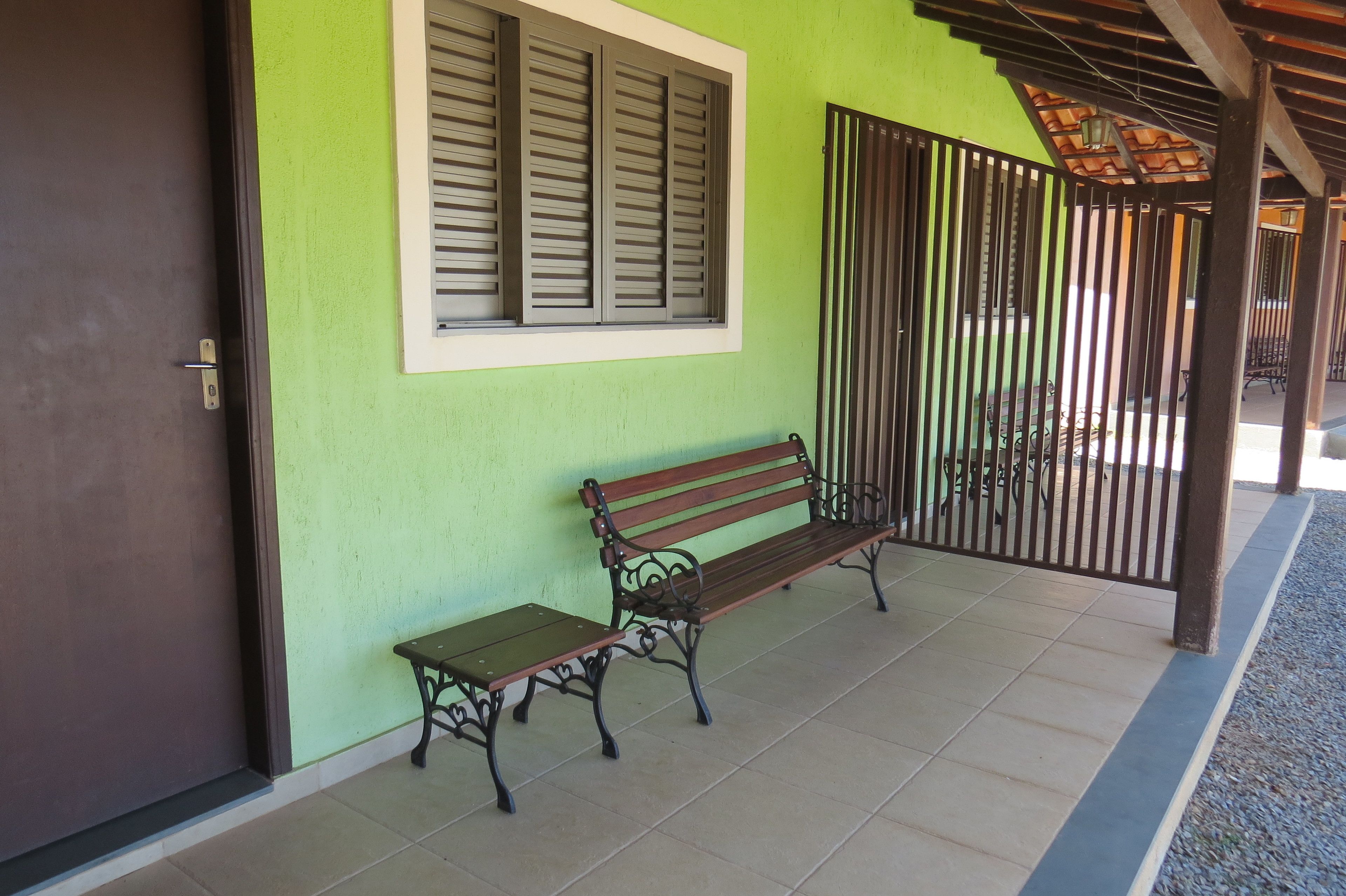 A bench and a table outside a building with a green wall and a window with shutters.