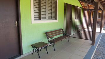 A bench and a table outside a building with a green wall and a window with shutters.