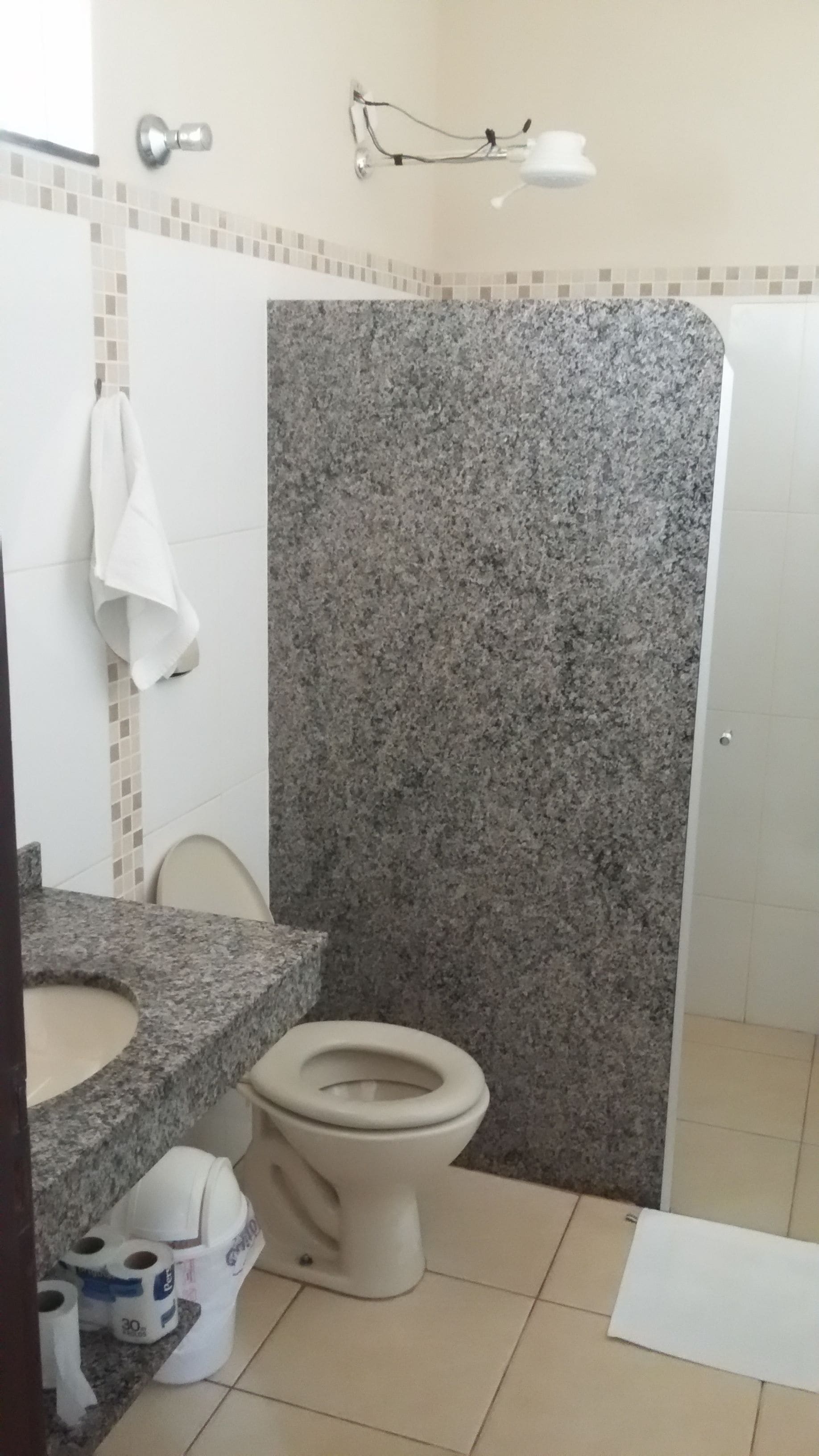 A bathroom with a granite countertop, a toilet, and a shower stall.