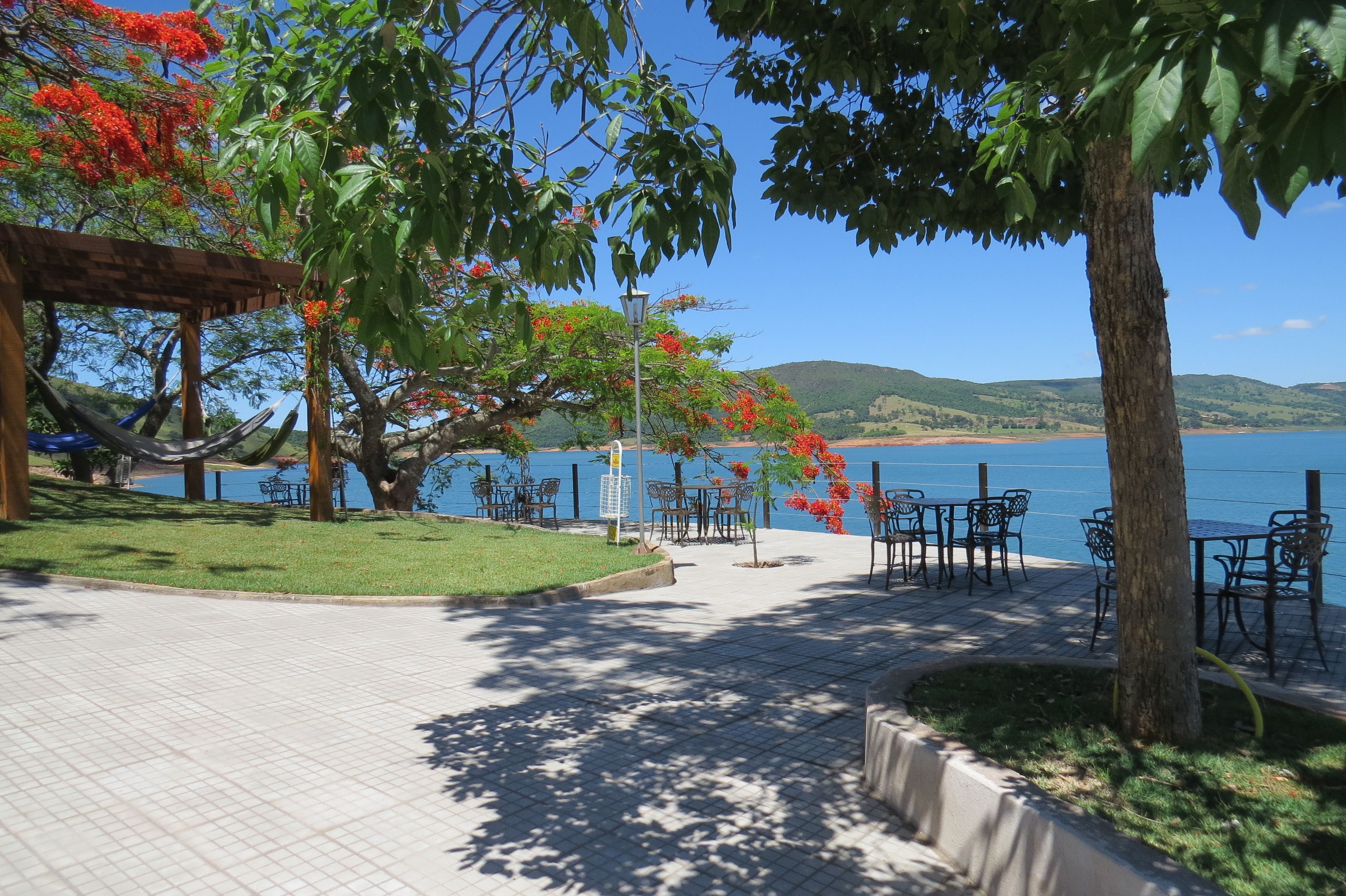 A waterfront patio with tables and chairs, a hammock, and a view of the sea and hills.