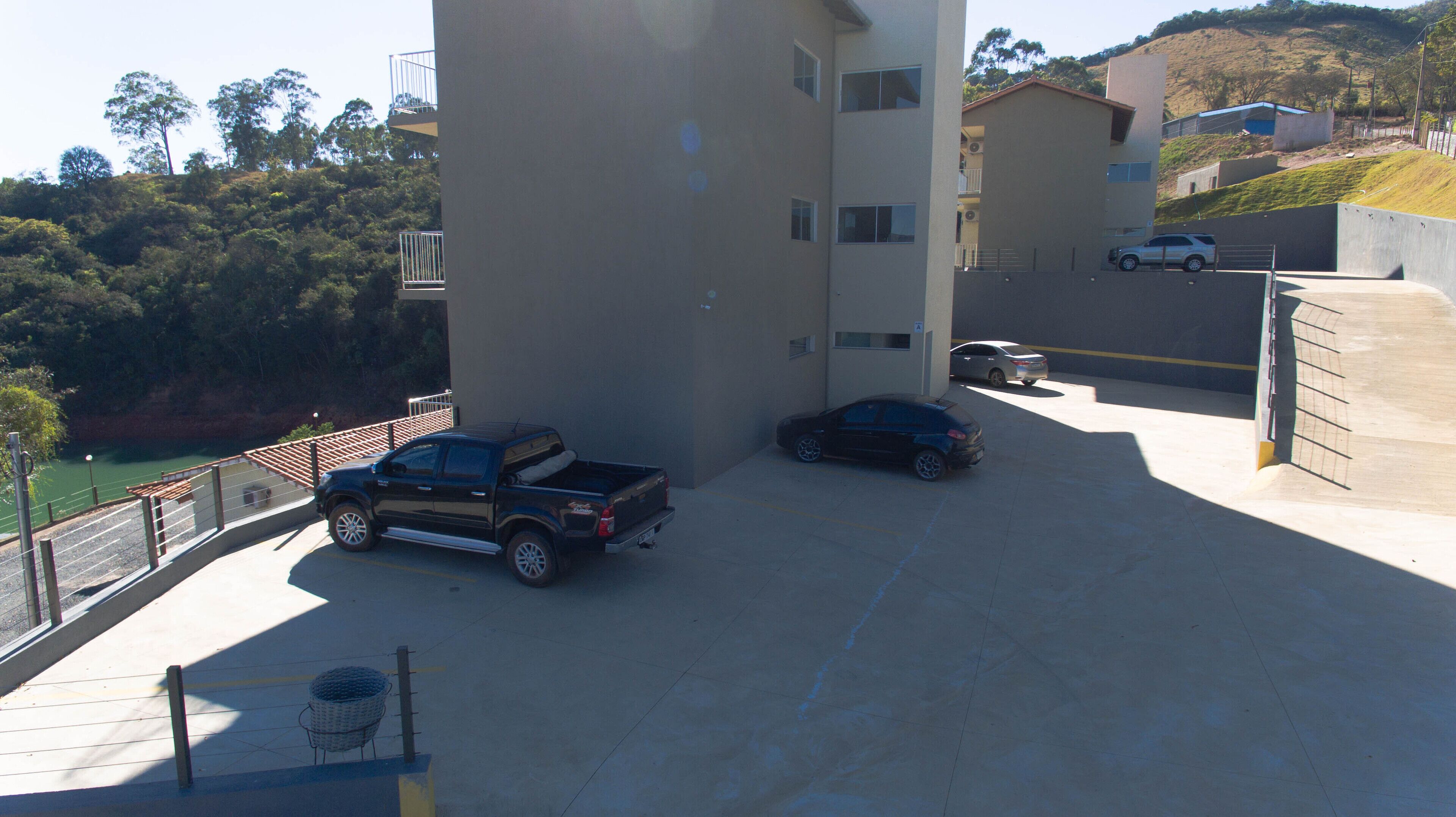 Un área de estacionamiento con una camioneta negra y un sedán negro, rodeado de edificios y una colina.