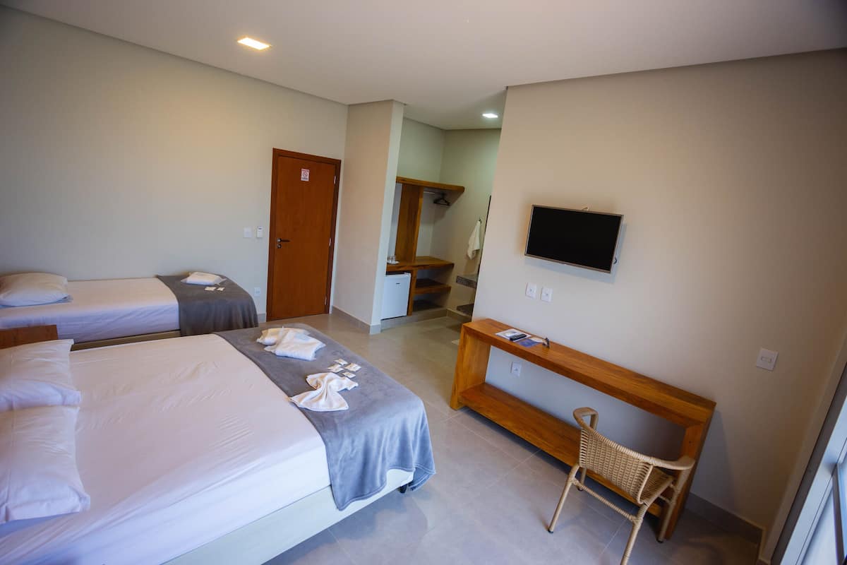 A hotel room with two beds, a TV, a wooden bench, and a mirror.