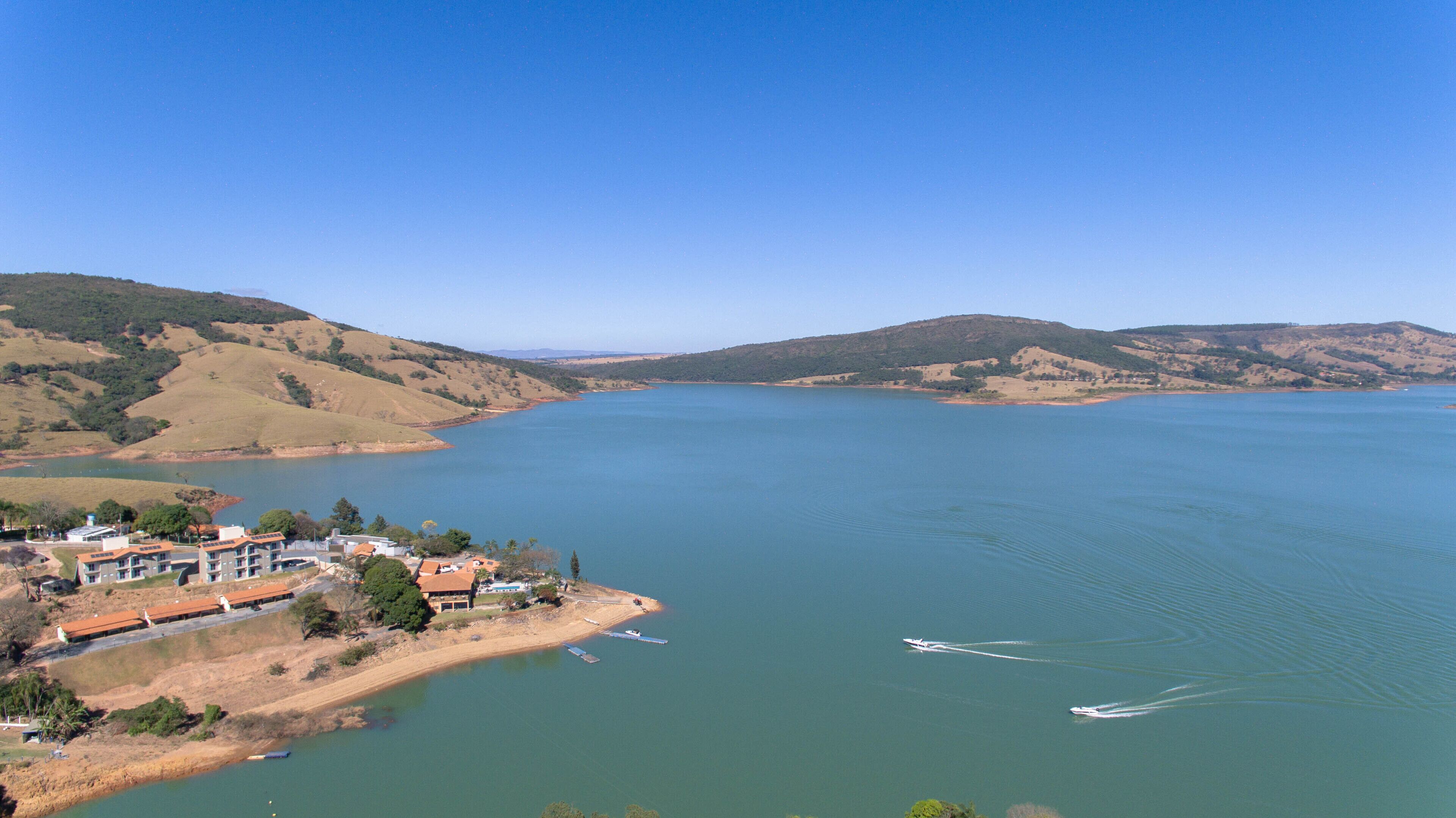 A large body of water surrounded by hills, with a small building complex on the left.