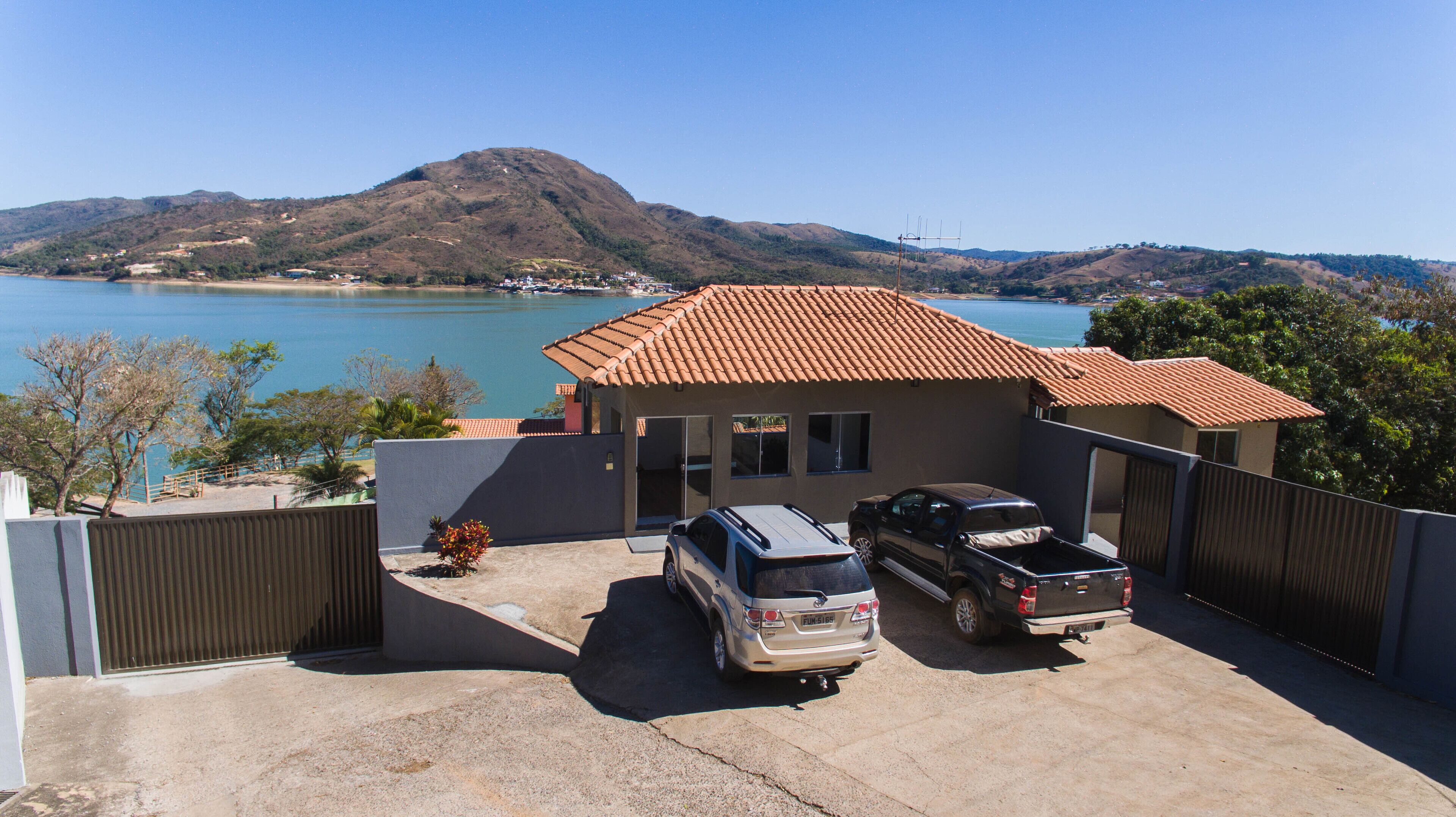 Una propiedad residencial con garaje, dos vehículos estacionados y vistas a un lago y colinas.