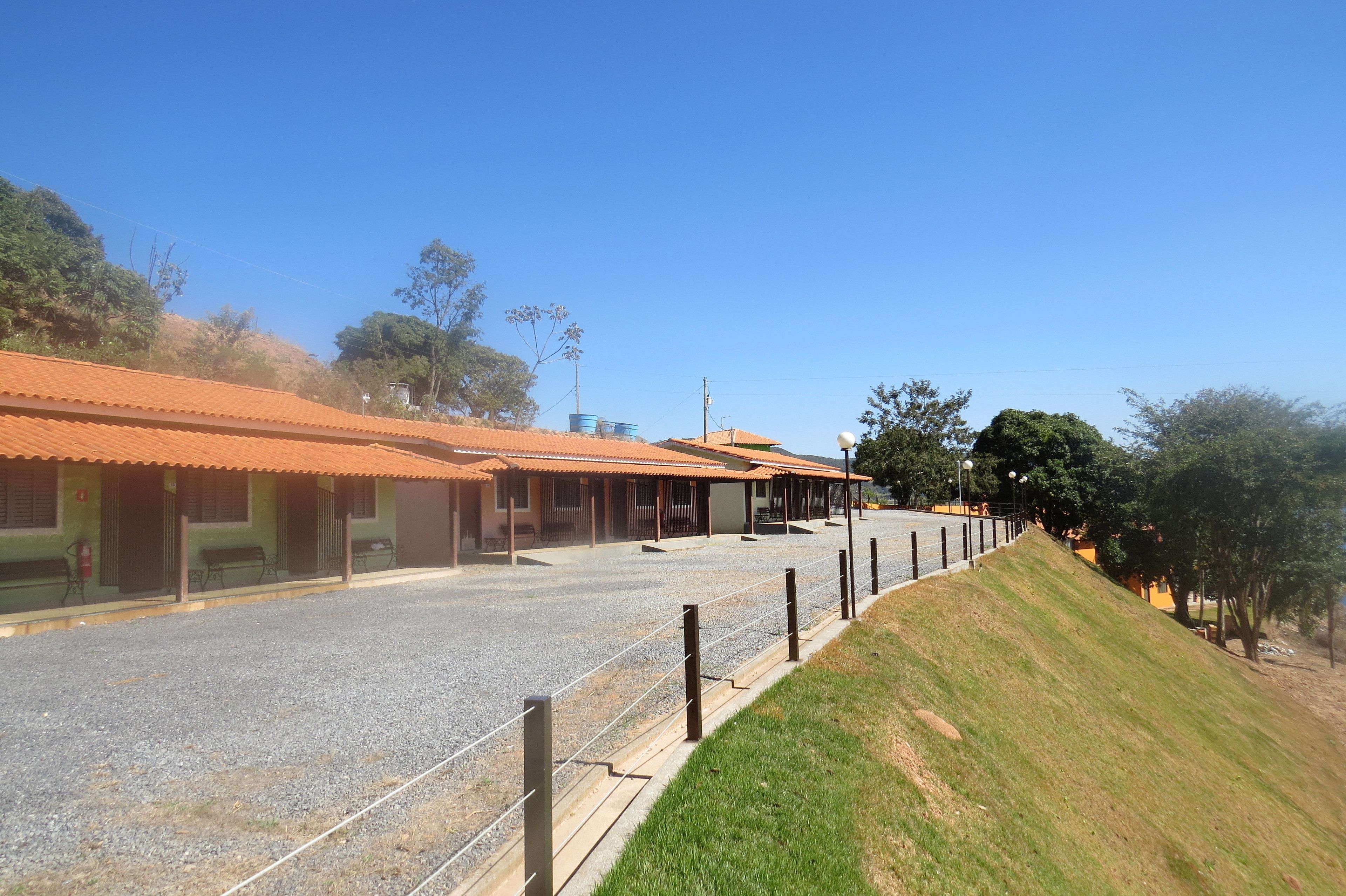 A building with a red-tiled roof, a gravel driveway, and a grassy hill.