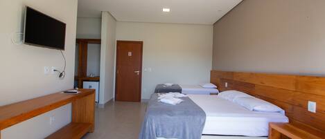 Ein Hotelzimmer mit einem großen Bett, einem an der Wand befestigten Fernseher, einer hölzernen Bank und einer Tür zu einem weiteren Raum.