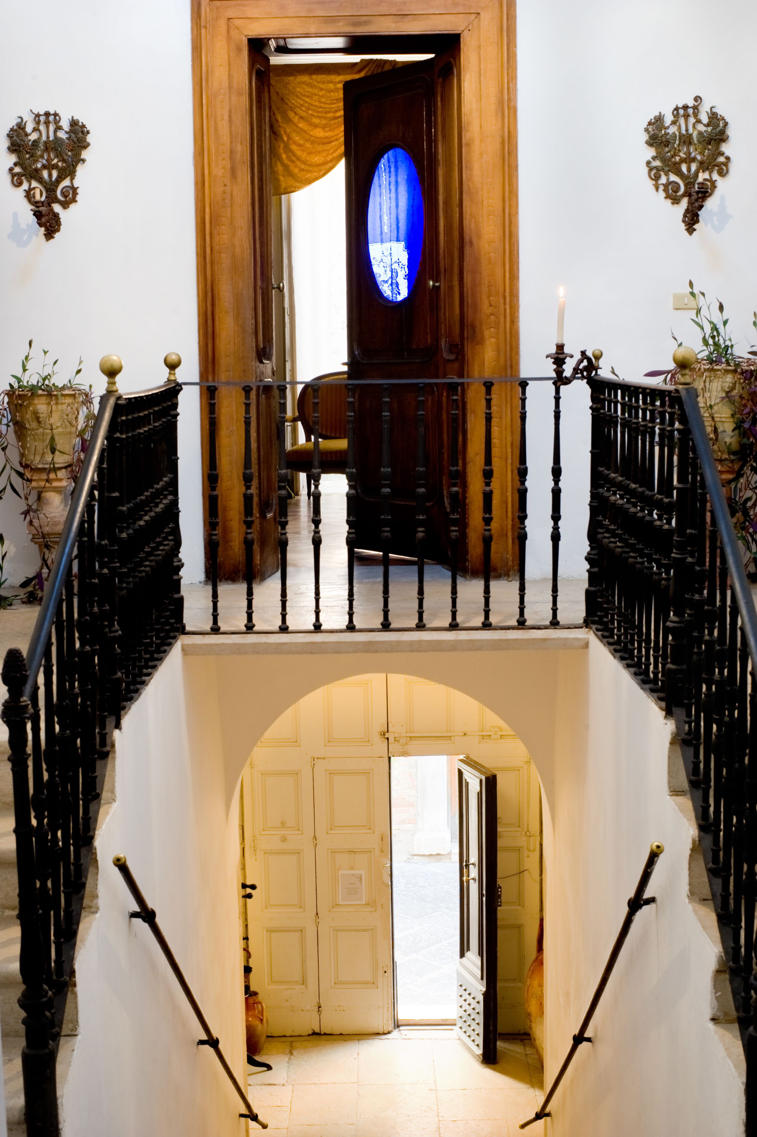 A grand staircase with a wooden finish and black balusters, leading to a room with a large window and a blue-tinted glass door.