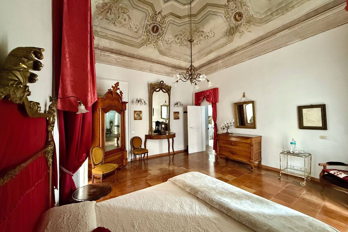 Ein geräumiges Zimmer mit einem großen Bett, einer Holzkommode, einem Spiegel und einem Kronleuchter.