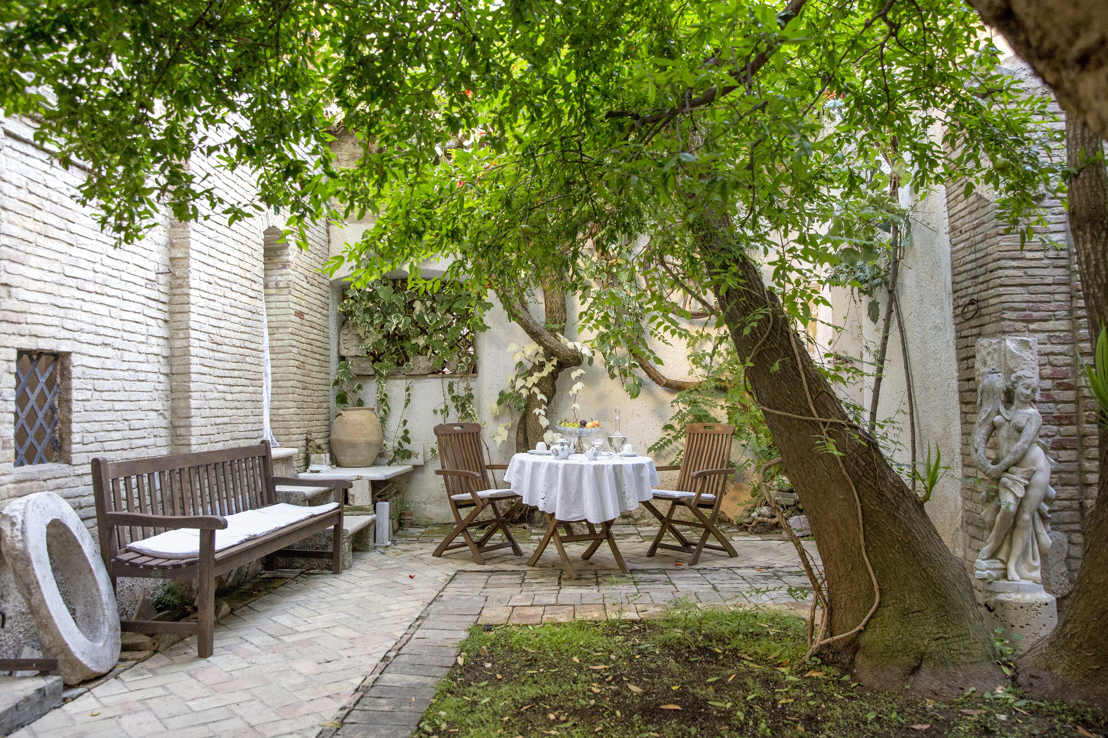 Une cour avec un banc en bois, une table avec des chaises et une statue.
