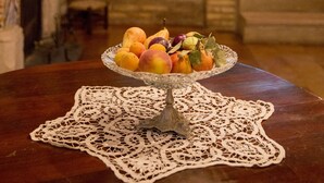 A dining table with a fruit centerpiece, a lace table runner, and a fireplace in the background. - Le Foglie di Acanto (Lucera)