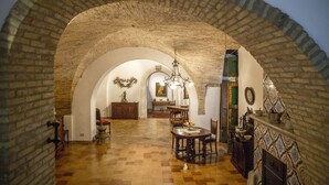 An arched stone corridor leading to a dining area with a checkered floor, wooden furniture, and a chandelier. - Le Foglie di Acanto (Lucera)