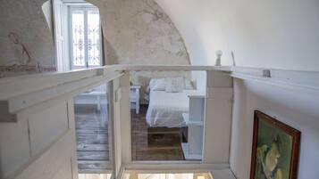 Una camera da letto con pavimento in legno, un letto con biancheria bianca, una finestra con inferriate decorative e un quadro appeso al muro.