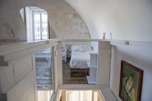 A bedroom with a wooden floor, a bed with white bedding, a window with decorative iron bars, and a painting on the wall. - Le Foglie di Acanto (Lucera)