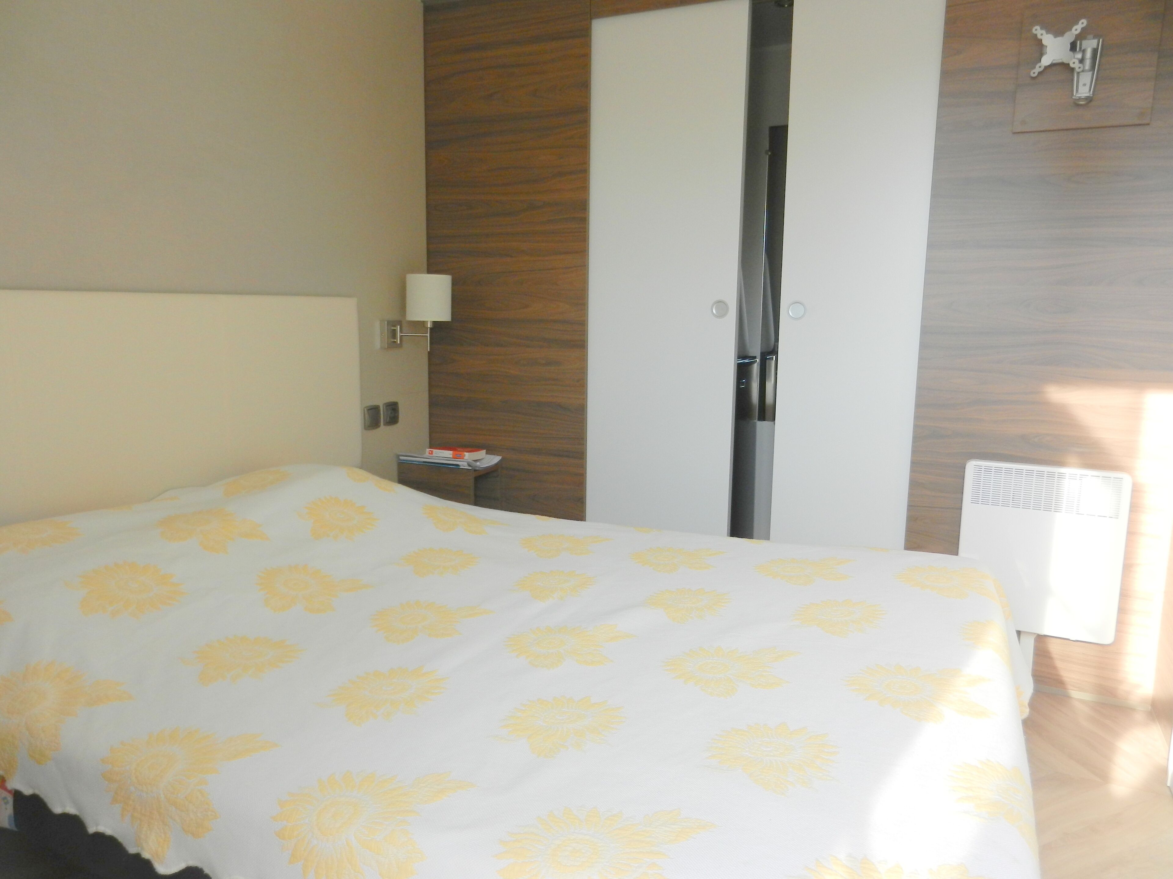 A hotel room with a bed, a nightstand, a lamp, a wardrobe, and a radiator.