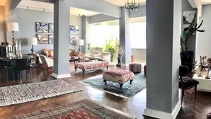 A spacious living room with hardwood floors, a large window, and a mix of seating including a sofa and ottomans. - Breathtaking Ocean View (Salvador)