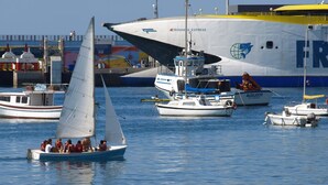 Eine Segelyacht mit Passagieren, vertäut neben einem großen Frachtschiff.