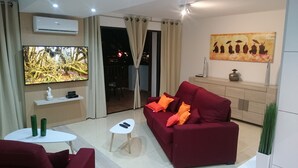 Ein modernes Wohnzimmer mit einem roten Sofa, einem Flachbildfernseher, einem kleinen weißen Tisch und einem Gemälde an der Wand.