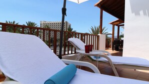 Ein Balkon mit weißen Lounge-Stühlen, einer blauen Yogamatte und roten Bechern auf einem kleinen Tisch.